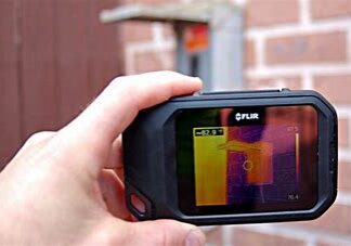 Hand holding a thermal imaging camera showing heat distribution.